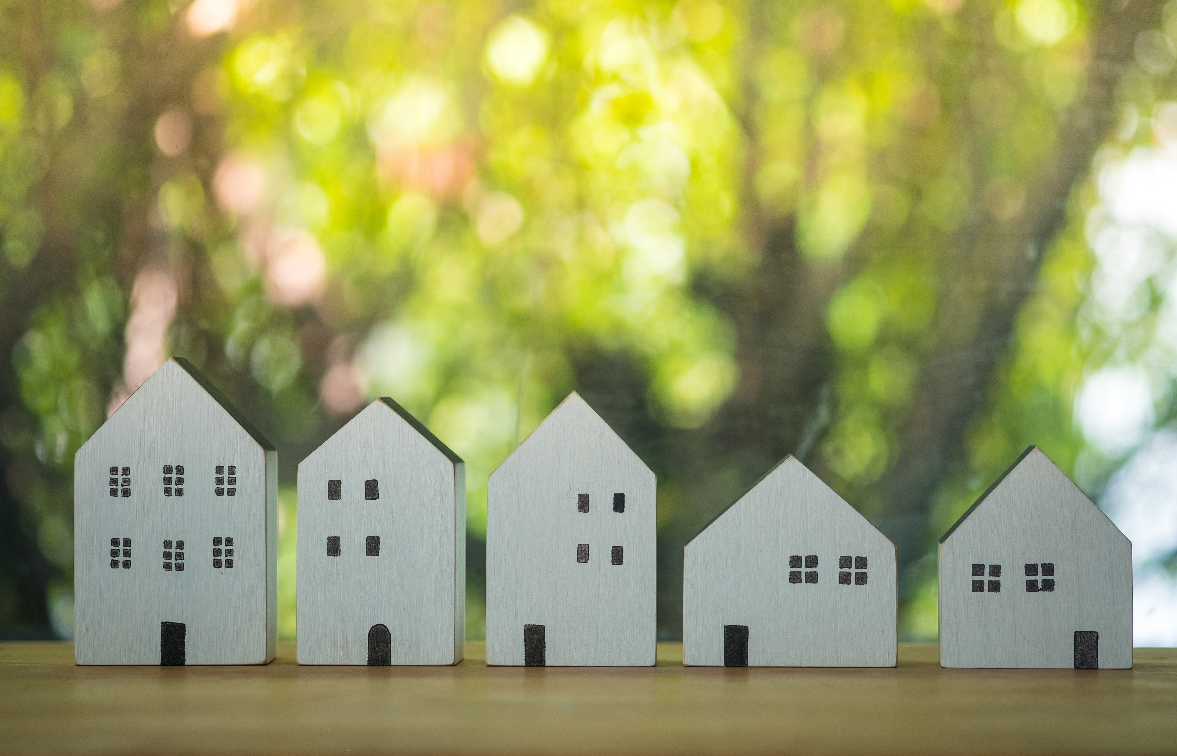 Differently sized wooden models of houses on table with green background. 